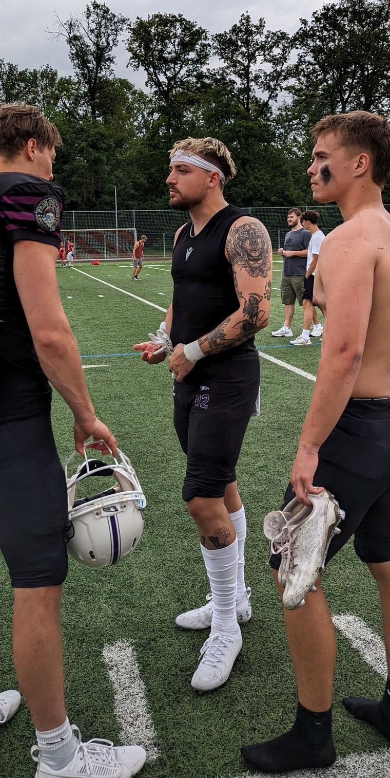 Nate Bock in training kit on a football field, talking with teammates.