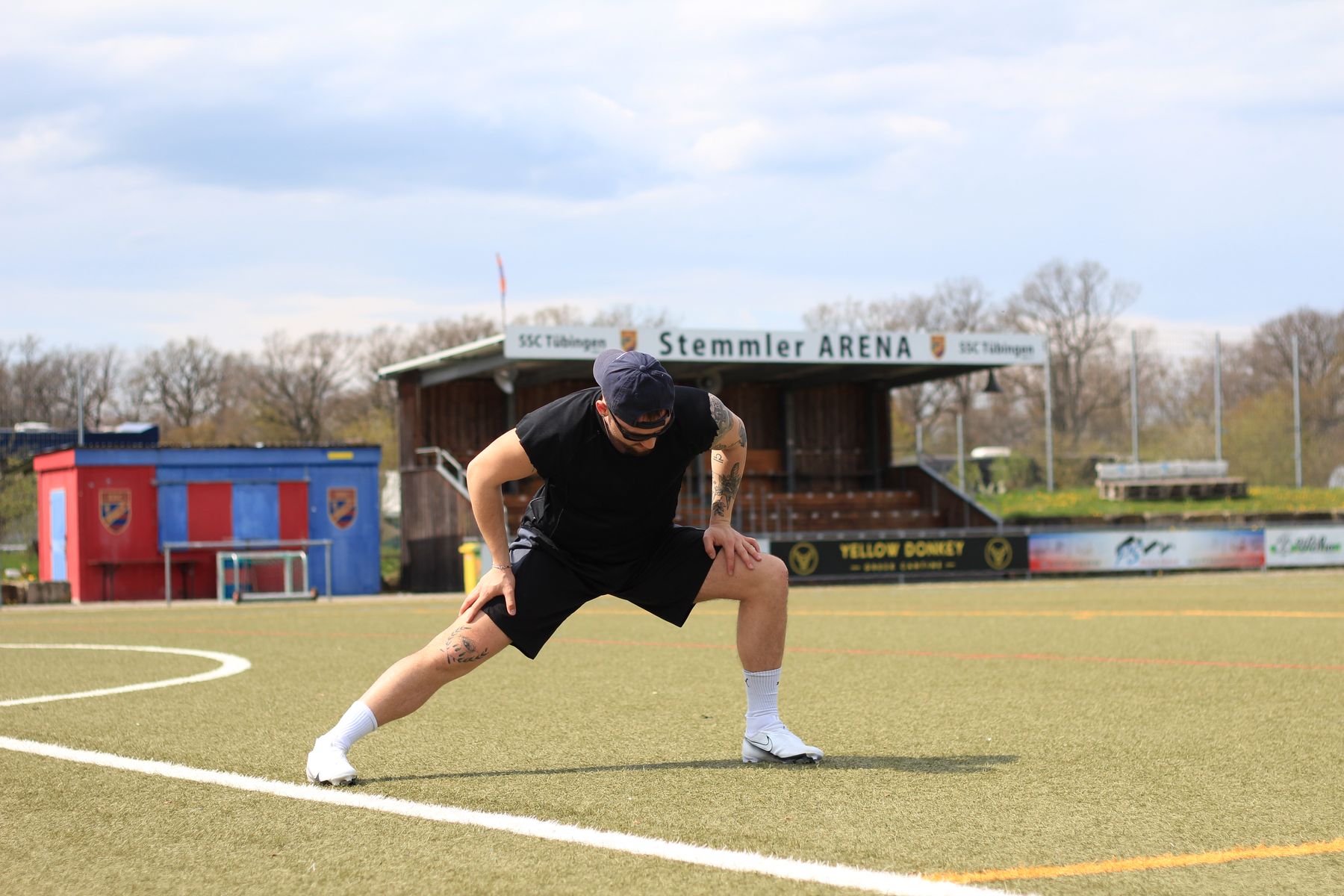 Nate Bock stretching on an artificial pitch in front of a small stadium stand.